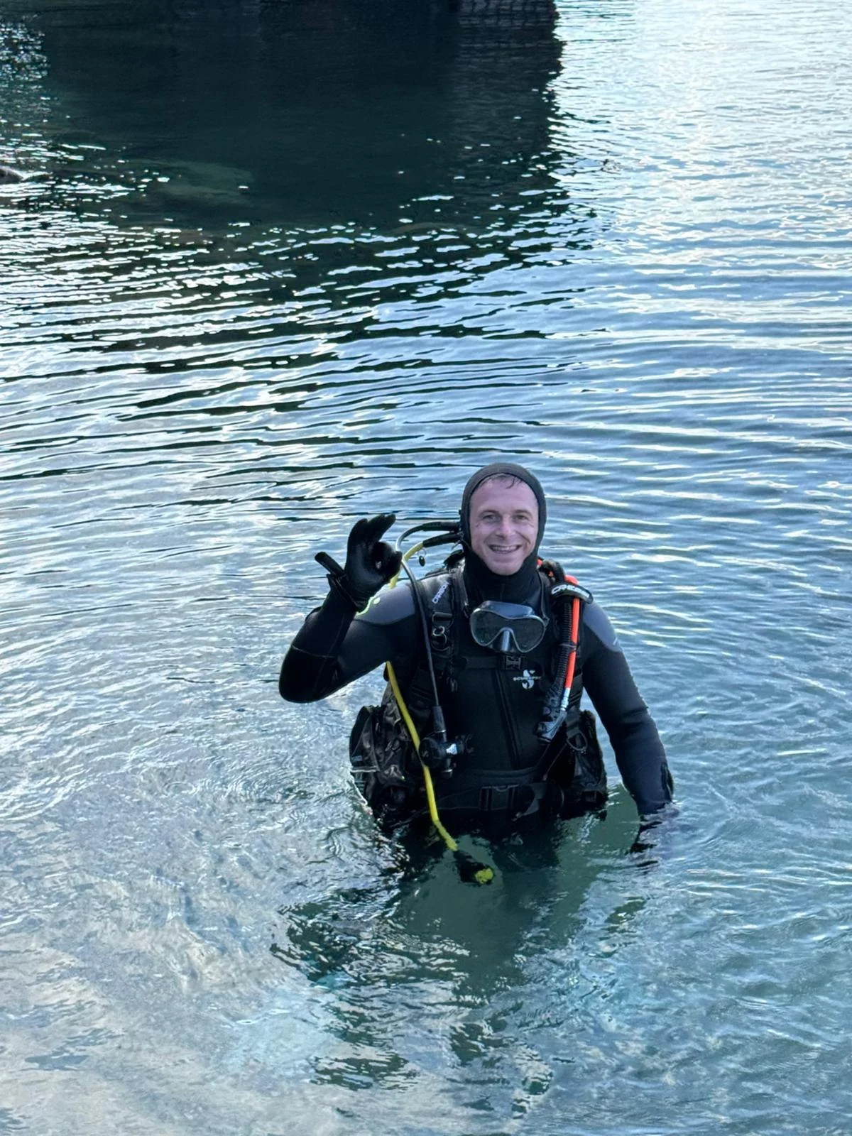Taucher im Wasser mit Ausrüstung Taucher steht im Wasser und zeigt ein Handzeichen, ausgestattet mit Tauchanzug und Atemgerät.