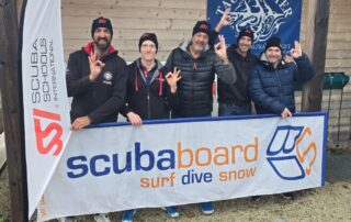 Fünf Taucher stehen vor einem Banner von Scubaboard und zeigen das Handzeichen für Tauchen.