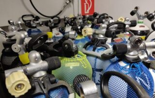 Tauchausrüstung mit mehreren Druckluftflaschen in verschiedenen Farben, die in Netzen aufbewahrt werden.