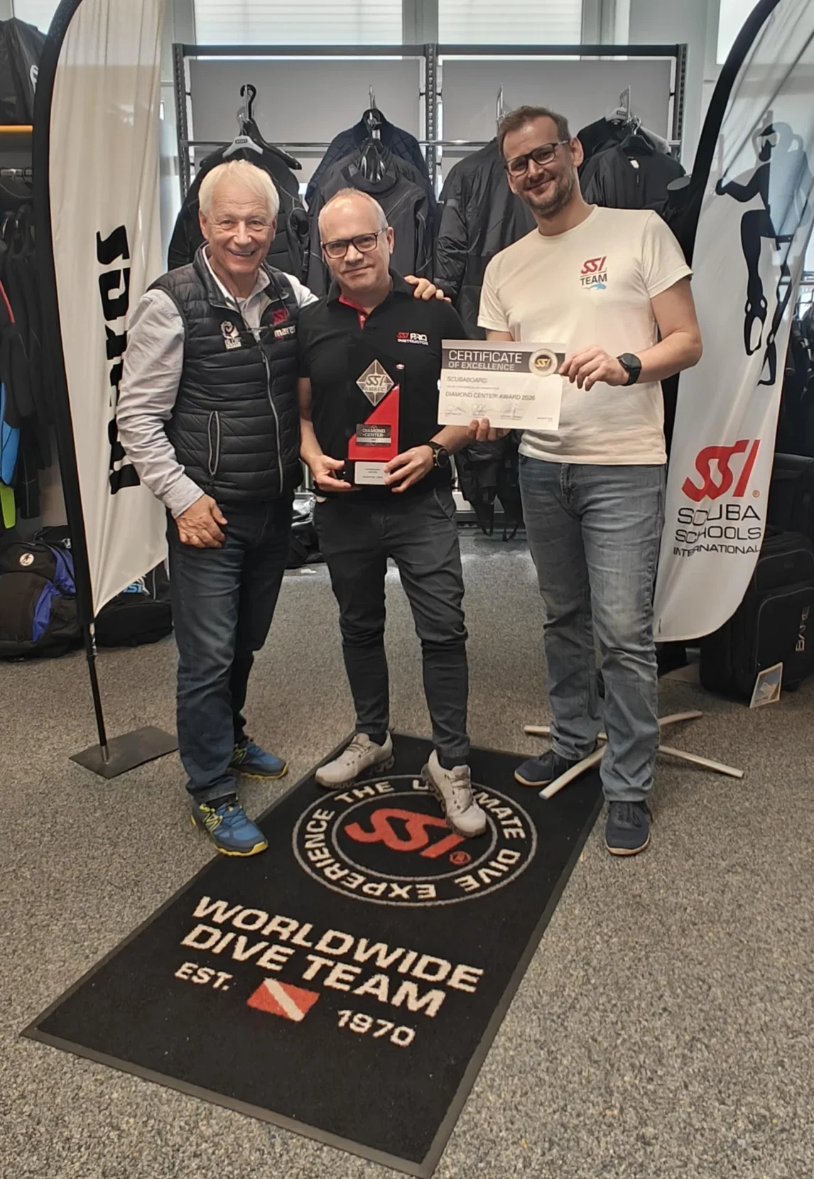 Beim SSI Diamond Center 2026 halten drei Männer gemeinsam ein Certificate of Excellence mit „SSI Team“ und 2026, im Innenbereich mit schwarzer, grauer und weißer Kleidung.