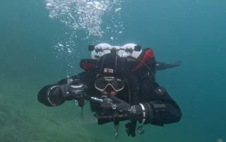 Beim XR Foundations Kurs taucht ein Taucher mit Doppelflaschen und Atemregler unter Wasser auf, umgeben von Luftblasen.