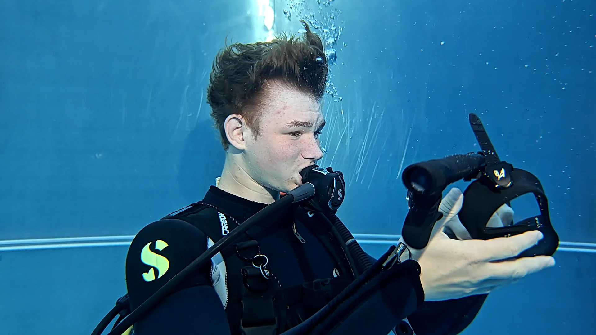 Open Water Diver Training im Attersee mit SSI Ausrüstung Ein junger Taucher übt unter Wasser mit Atemregler und Tauchmaske im blauen See vor hellem Hintergrund.