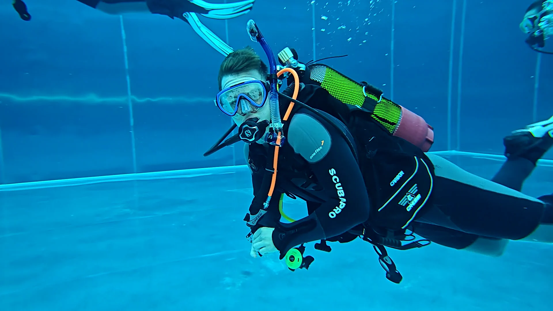 Open Water Diver im Pooltraining mit SSI-Ausrüstung Ein Taucher im schwarzen Neoprenanzug mit blauer Maske und Flasche schwebt im Poolwasser beim Training.