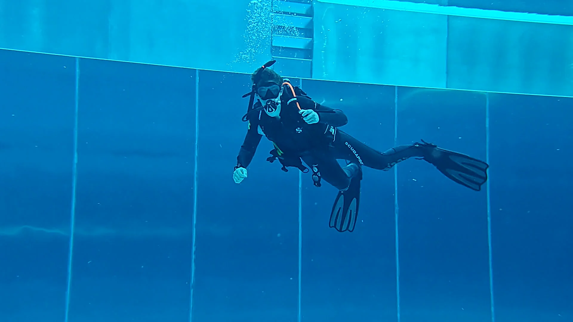 Scubaboard Taucher im Pool mit schwarzer Ausrüstung Ein Taucher mit Maske, Flossen und Tauchflasche schwebt in blauem Wasser vor der Beckenwand und hält die Trimmung ruhig.