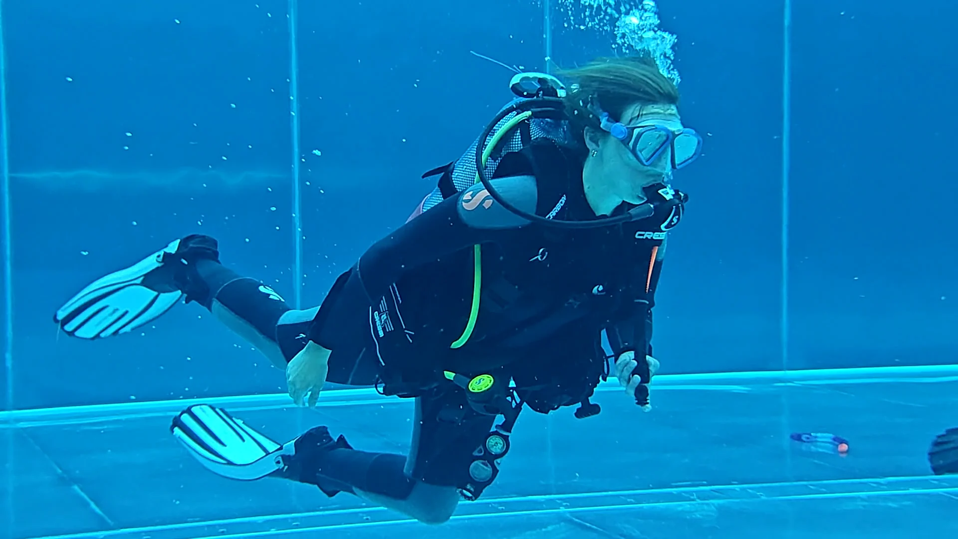 Taucherin im Pooltraining mit Flossen und Atemregler, Scubaboard Eine Taucherin in schwarzer Ausrüstung übt im blauen Poolwasser mit Flossen, Atemregler und Tauchflasche.