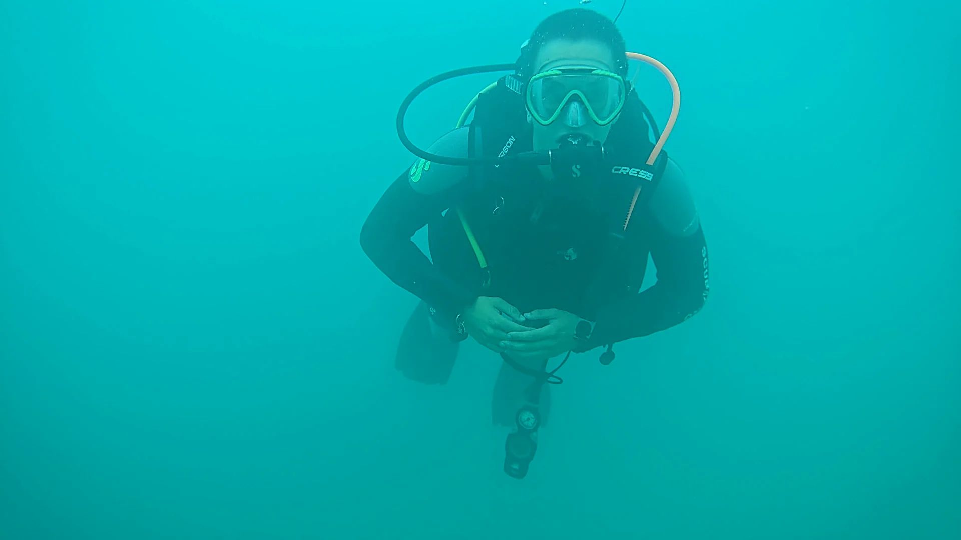 Taucher im türkisfarbenen Freiwasser beim Open Water Diver Abschluss Ein Taucher schwebt im türkisfarbenen Freiwasser mit Maske, Regler, Tauchanzug und Atemflasche vor der Kamera.