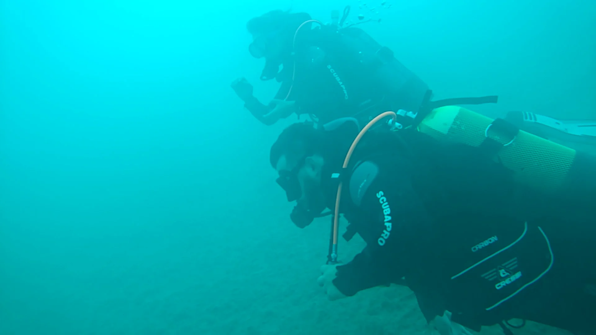 Zwei Taucher beim Freiwassertauchgang am Attersee mit Scubaboard Zwei Taucher in Scubaboard-Tauchanzügen bewegen sich im trüben, türkisfarbenen Wasser des Attersees nebeneinander voran.