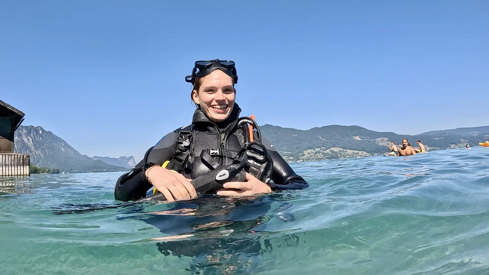 GPTempDownload-11 Eine lächelnde Taucherin im schwarzen Neoprenanzug hält sich im klaren Seewasser über Wasser.
